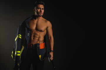 young handsome adult, muscular firefighter in uniform holding ax of fire equipment in his hands,...