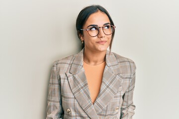 Young brunette woman wearing business jacket and glasses smiling looking to the side and staring away thinking.