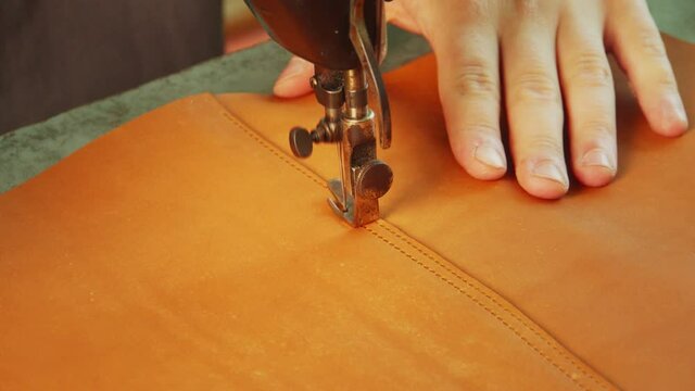 Slow-motion video a sewing machine makes a stitch with a thread on a leather bag. Close-up of the tailor's hand.
