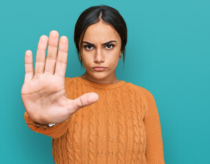 Young brunette woman wearing casual winter sweater doing stop sing with palm of the hand. warning...