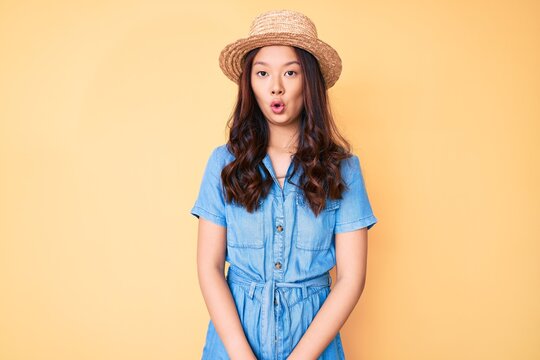 Young beautiful chinese girl wearing summer hat afraid and shocked with surprise expression, fear and excited face.