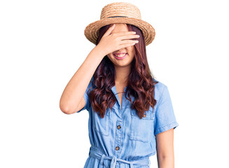 Young beautiful chinese girl wearing summer hat smiling and laughing with hand on face covering eyes for surprise. blind concept.