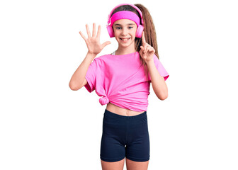 Obraz na płótnie Canvas Cute hispanic child girl wearing gym clothes and using headphones showing and pointing up with fingers number six while smiling confident and happy.