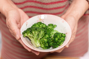 ブロッコリーの入った器を持つ女性の手元クローズアップ。農業と自然の恵みｔ温野菜。ヘルシーな食生活