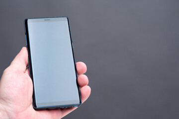 Smartphone in a man's hand. Mobile phone next to the place for text. A person is holding a smartphone with a blank screen. A man shows a smartphone in an upright position.