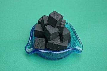  black square charcoal for a hookah in a blue glass ashtray stands on a green background