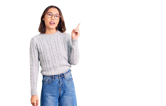 Young beautiful chinese girl wearing casual clothes pointing finger up with successful idea. exited and happy. number one.