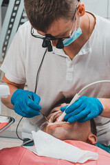 Dentist in the clinic,tartar removal procedure,the dentist in binoculars removes tartar in the patient's mouth.