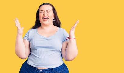 Young plus size woman wearing casual clothes celebrating mad and crazy for success with arms raised...
