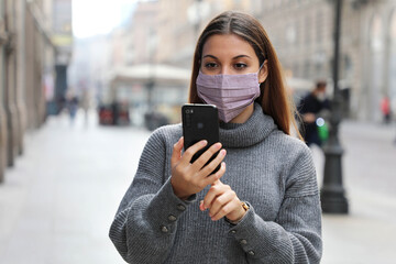 Young business woman sending message on mobile phone in city street wearing face mask protection