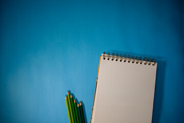 Notebook with a set of colored pencils with the range of greens. Light blue background