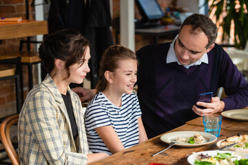Family, parenthood, communication and people concept - happy mother, father and their girl having dinner and talking at a restaurant or cafe.