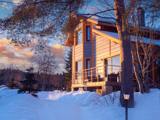 Cottage with open veranda is illuminated by the setting sun. End of a winter day in the countryside. Private house against a beautiful sky. Two-storey country house with panoramic Windows.