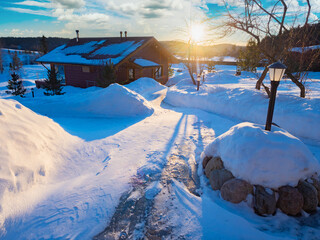 Winter landscape with sunset. The snow-covered paths are illuminated by the setting sun. Winter outside the city. Cottage in the snow and the setting sun.