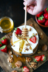 Camembert cheese with strawberries and nuts. A honey stick pours honey on a Camembert. Healthy dessert. An exquisite beautiful dessert.