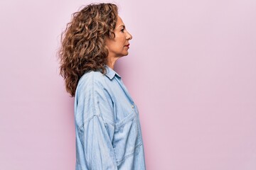 Middle age beautiful woman wearing casual denim shirt standing over pink background looking to side, relax profile pose with natural face and confident smile.