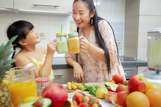 Happy asian family mother and her daughter enjoy prepare freshly squeezed fruits with vegetables for making smoothies for breakfast together in the kitchen.diet and Health concept.