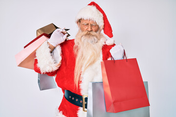 Old senior man with grey hair and long beard wearing santa claus costume holding shopping bags skeptic and nervous, frowning upset because of problem. negative person.