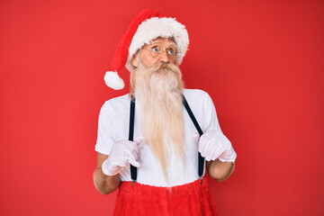 Old senior man wearing santa claus costume with suspenders smiling looking to the side and staring away thinking.