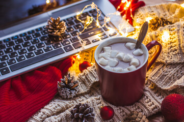 Obraz na płótnie Canvas Red Cup with cocoa and marshmallows on the table with a scarf laptop and online shopping Christmas