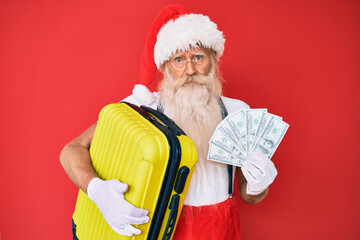 Old senior man with grey hair and long beard wearing santa claus costume holding dollars and suitcase depressed and worry for distress, crying angry and afraid. sad expression.