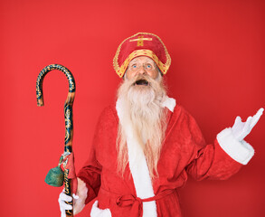 Old senior man with grey hair and long beard wearing traditional saint nicholas costume crazy and...