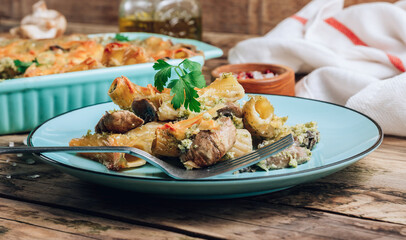 Casserole with pasta, mushrooms, broccoli sauce and cheese on a rustic wooden background.