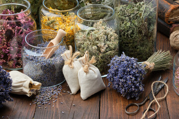 Glass jars of dry different medicinal herbs, aromatic sachets, bunches of dry lavender on table....