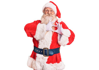 Old senior man with grey hair and long beard wearing traditional santa claus costume smiling in love doing heart symbol shape with hands. romantic concept.