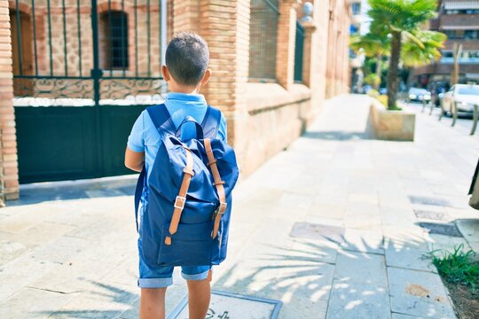 Adorable student boy on back view wearing backpack at street of city.