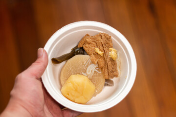 紙皿に盛ったおでんを持つ手。日本文化と食生活、冬の風物詩