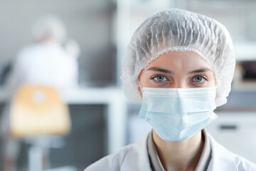 Close up portrait of young female medic wearing face mask and looking at camera while working in...