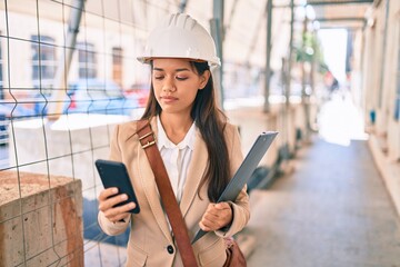 Young latin architect girl with serious expression using smartphone at the city.