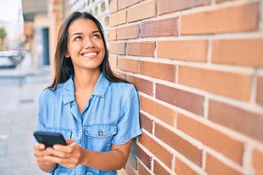 Young latin girl smiling happy using smartphone at the city.