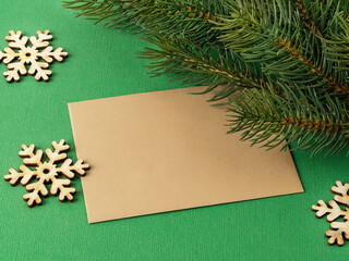 Fototapeta na wymiar Blank brown greeting card, few wooden snowflakes and spruce branch on a textured green background. Winter season holidays Christmas and New Year. Copy space.