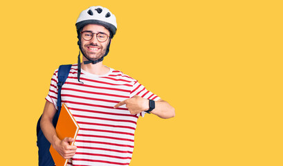 Young hispanic man wearing student backpack and bike helmet holding binder pointing finger to one self smiling happy and proud