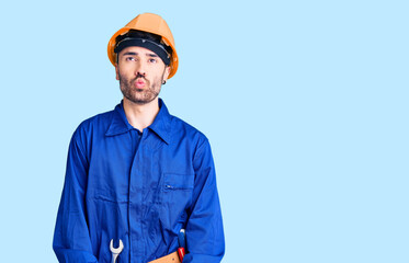 Young hispanic man wearing worker uniform making fish face with lips, crazy and comical gesture. funny expression.