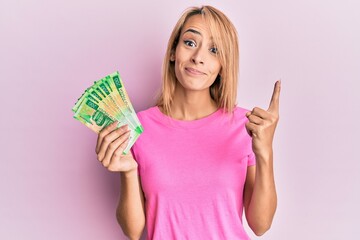 Beautiful blonde woman holding 200 russian ruble banknotes smiling with an idea or question pointing finger with happy face, number one