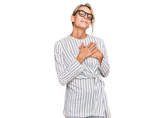 Beautiful blonde woman wearing business shirt and glasses smiling with hands on chest with closed eyes and grateful gesture on face. health concept.