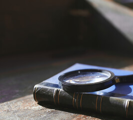 Old book and magnifying glass on table