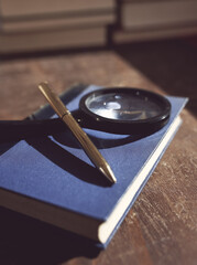Old book with magnifying glass and pen on table