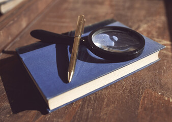 Old book with magnifying glass and pen on table