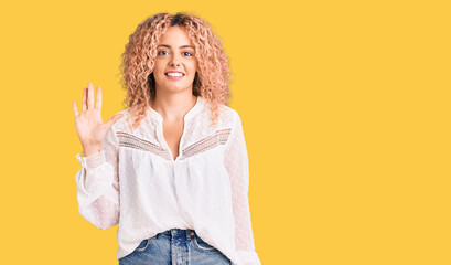 Young blonde woman with curly hair wearing elegant summer shirt showing and pointing up with fingers number five while smiling confident and happy.