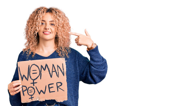 Young blonde woman with curly hair holding we need a change banner pointing finger to one self smiling happy and proud
