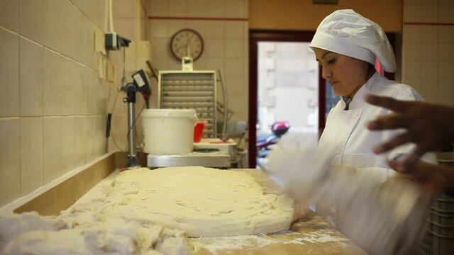 Skilled hispanic female baker with male assistant preparing shaped raw dough for proofing before baking. High quality FullHD footage