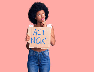 Young african american woman holding act now banner serious face thinking about question with hand on chin, thoughtful about confusing idea