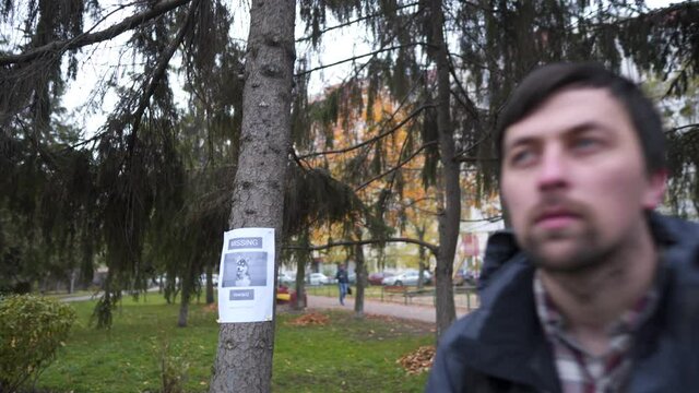 In search of lost domestic husky dog in city, adult Caucasian man calls puppy, attracting attention with treat for animals in city park in autumn cloudy weather. Responsible attitude to animals