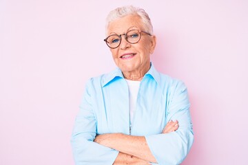 Senior beautiful woman with blue eyes and grey hair wearing glasses happy face smiling with crossed arms looking at the camera. positive person.