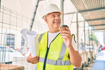 Middle age architect man holding blueprints and drinking take away coffee at the city.