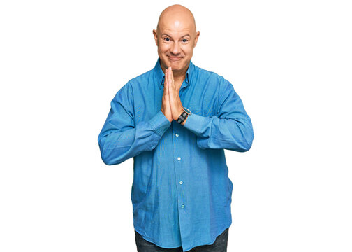 Middle age bald man wearing casual clothes praying with hands together asking for forgiveness smiling confident.